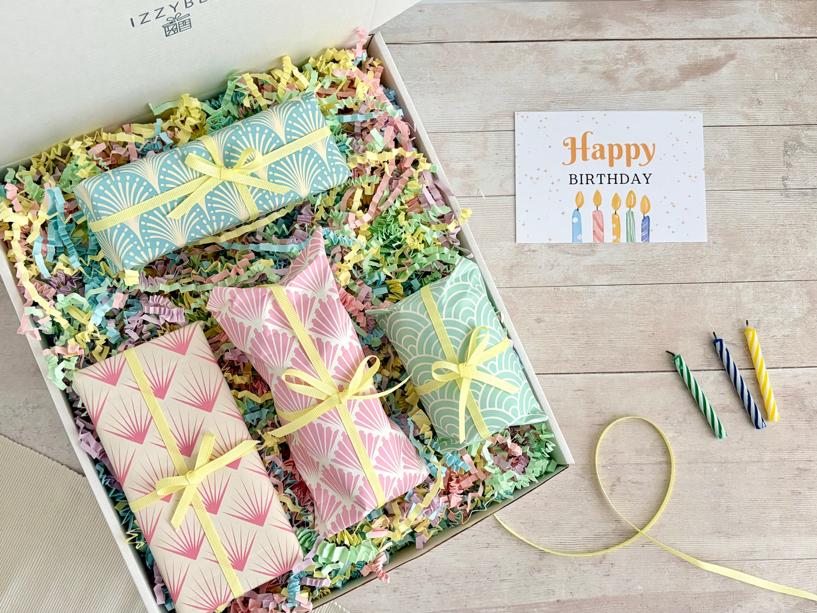 Birthday Surprise Gift Hamper with four individually wrapped gifts with pastel art deco patterns in different colours and yellow ribbon in gift box with multicoloured paper shred