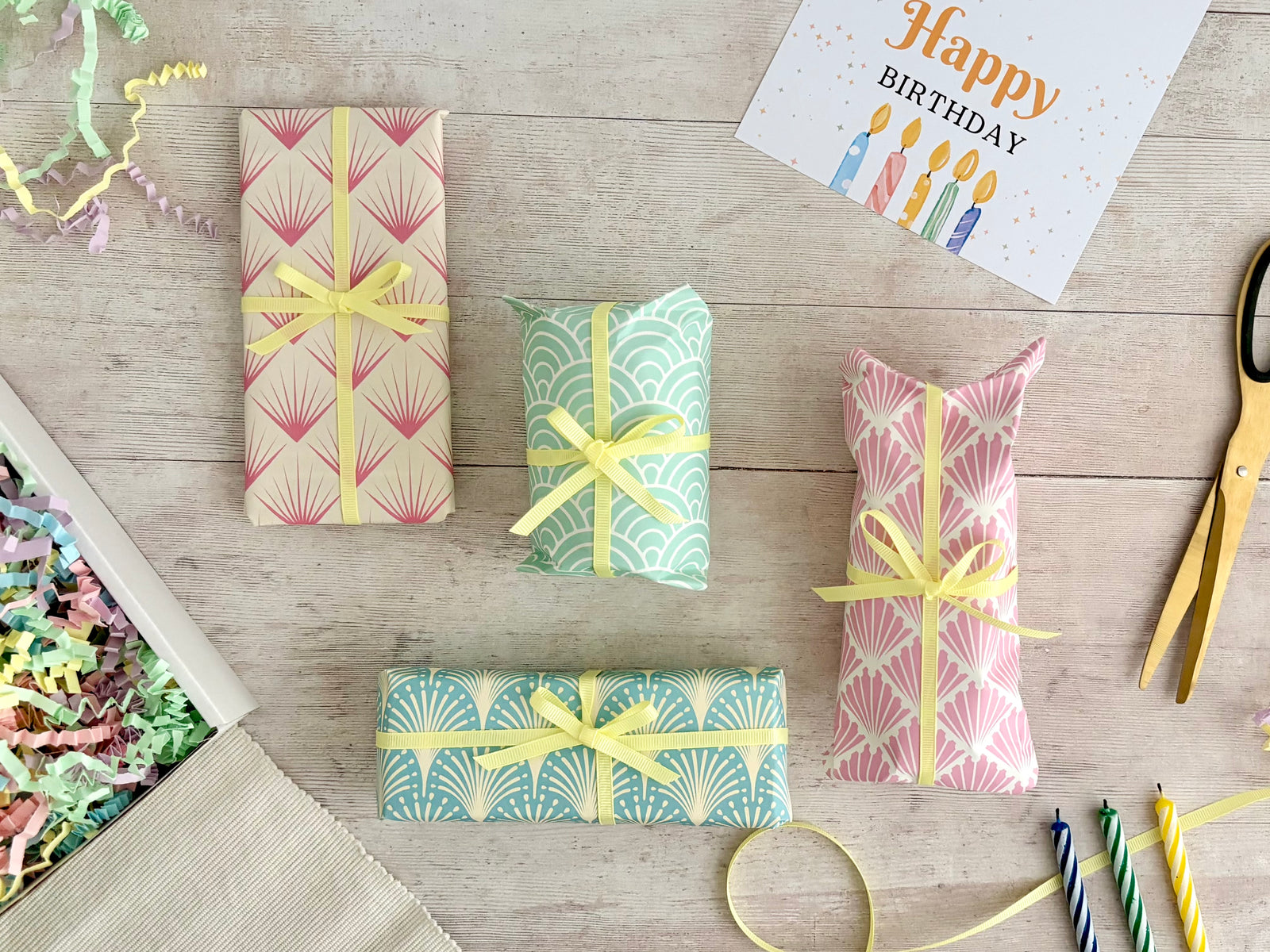 Birthday Surprise Gift Hamper with four individually wrapped gifts with pastel art deco patterns in different colours and yellow ribbon in gift box with multicoloured paper shred