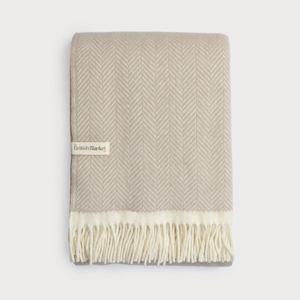 Beige and white herringbone patterned blanket with fringes on a light gray background