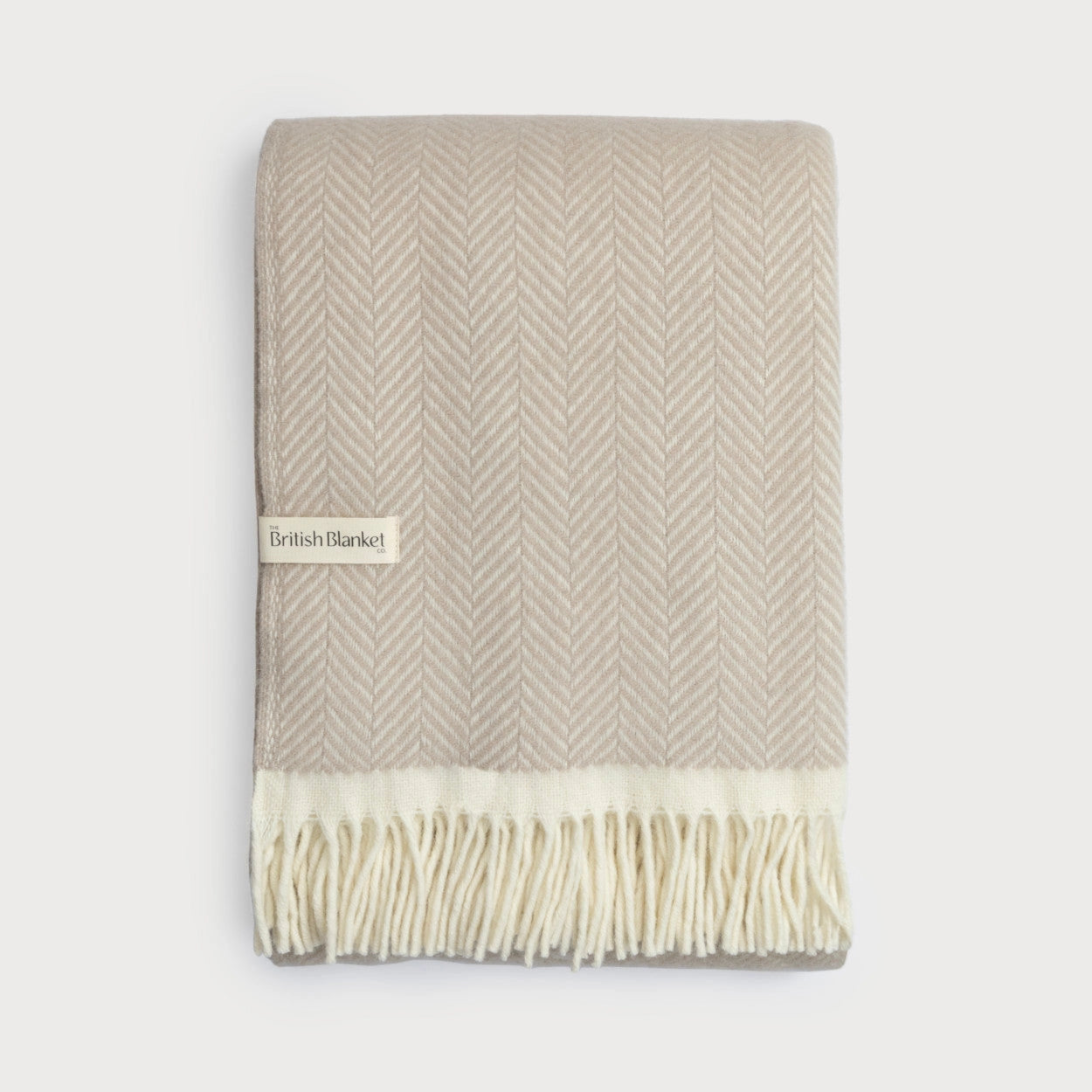 Beige and white herringbone patterned blanket with fringes on a light gray background