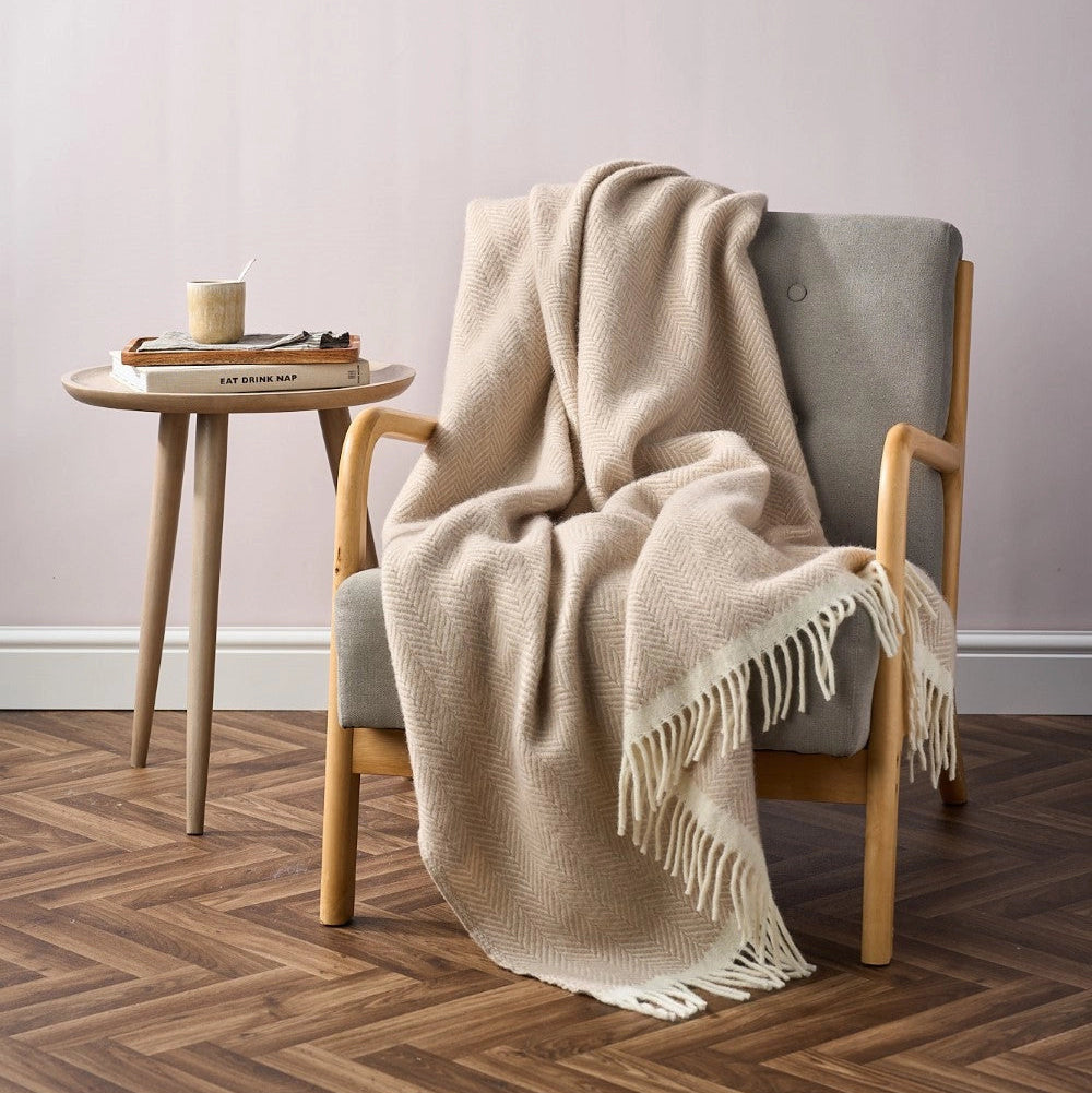Beige and white herringbone patterned blanket with fringes on a light gray background