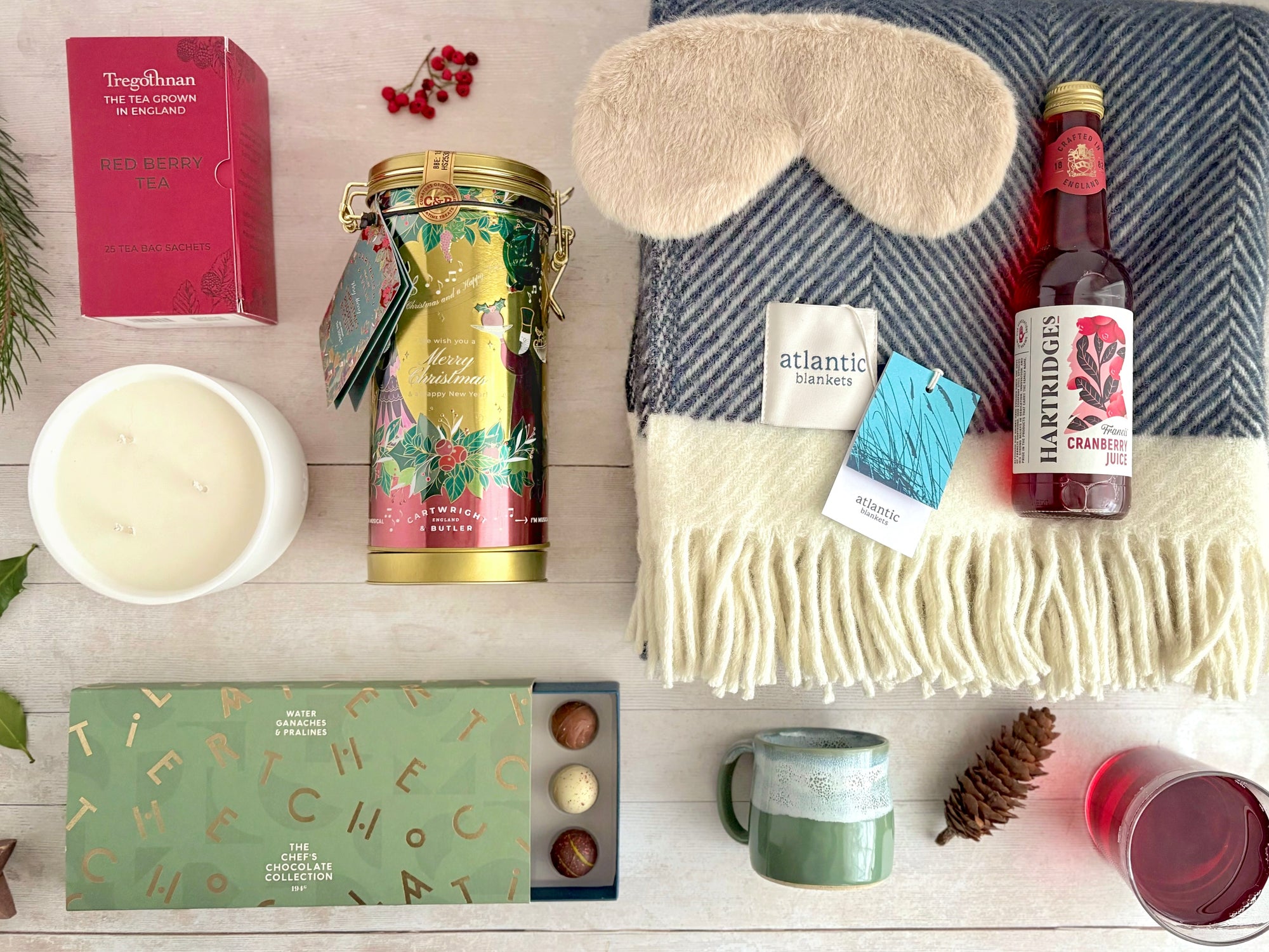 Christmas Home Hamper with Wool Navy Herringbone Blanket, fluffy eye mask, luxury chocolates, handmade pottery muglet in sage, musical merry christmas biscuit tin, triple wick handpoured candle in clay pot, red berry Cornwall-grown tea.