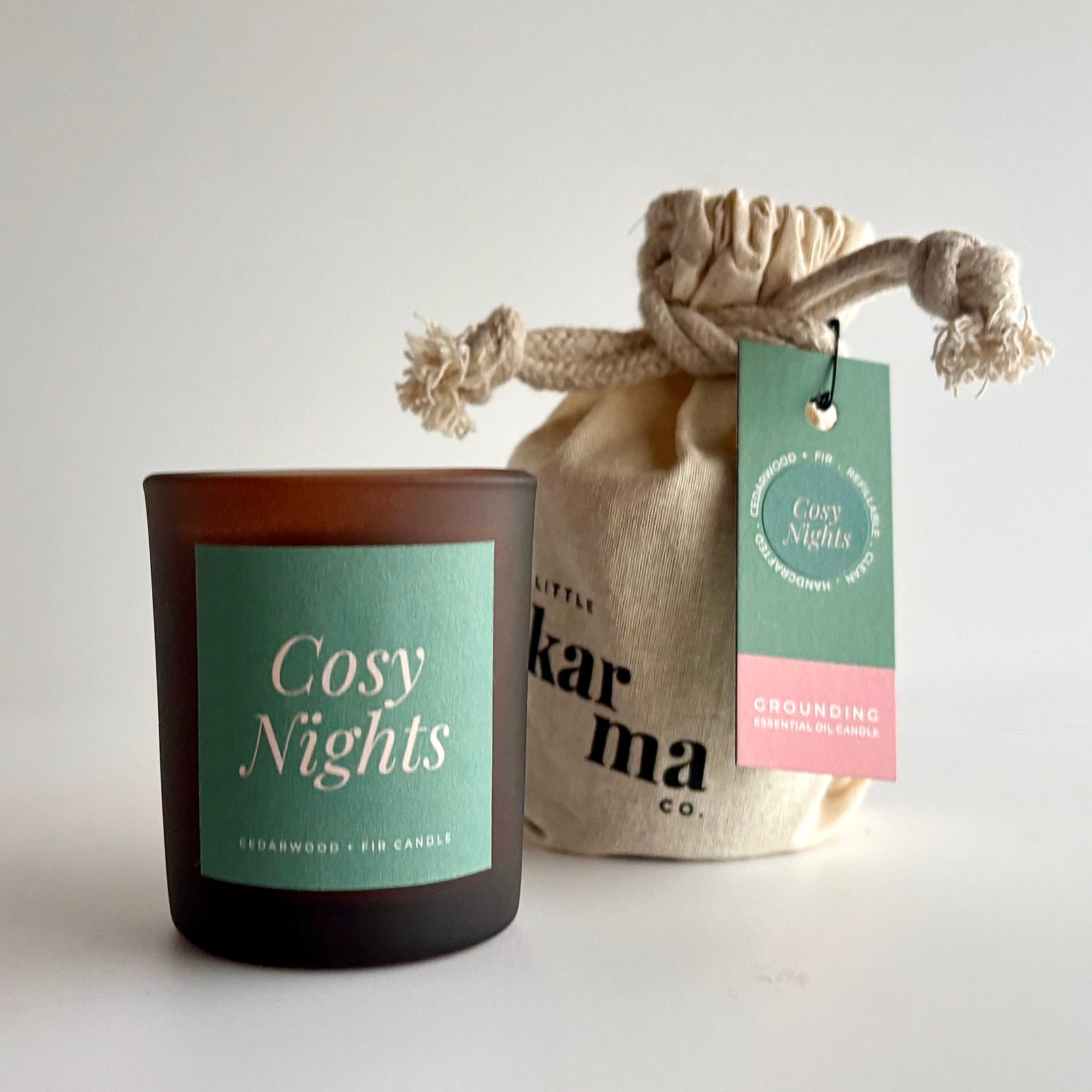 A frosted amber glass candle jar labeled 'Cosy Nights' with a mint green label, placed in front of a beige fabric drawstring pouch