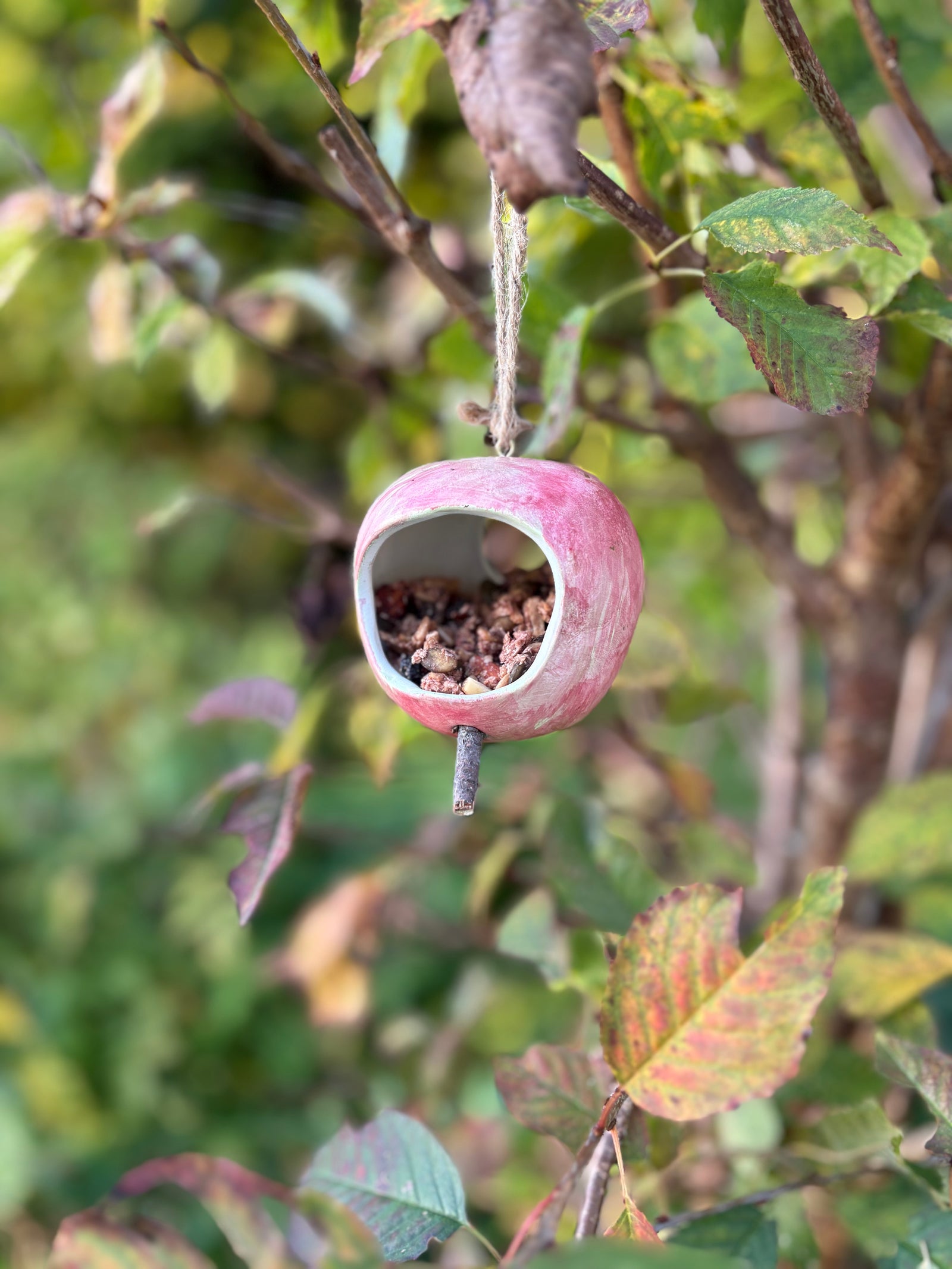Ceramic apple hanging from a tree branch with leaves and twigs in the background