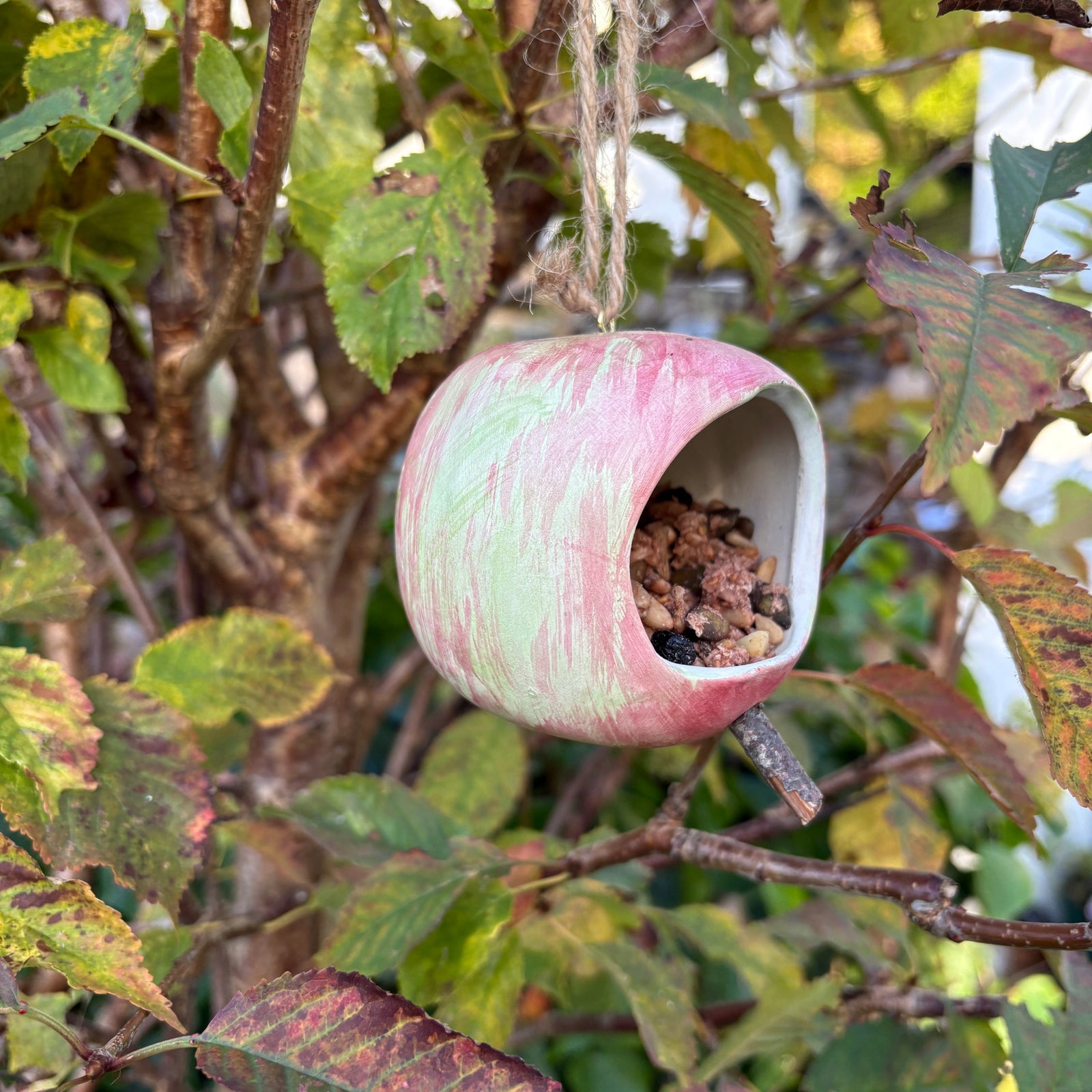 Ceramic apple hanging from a tree branch with leaves and twigs in the background