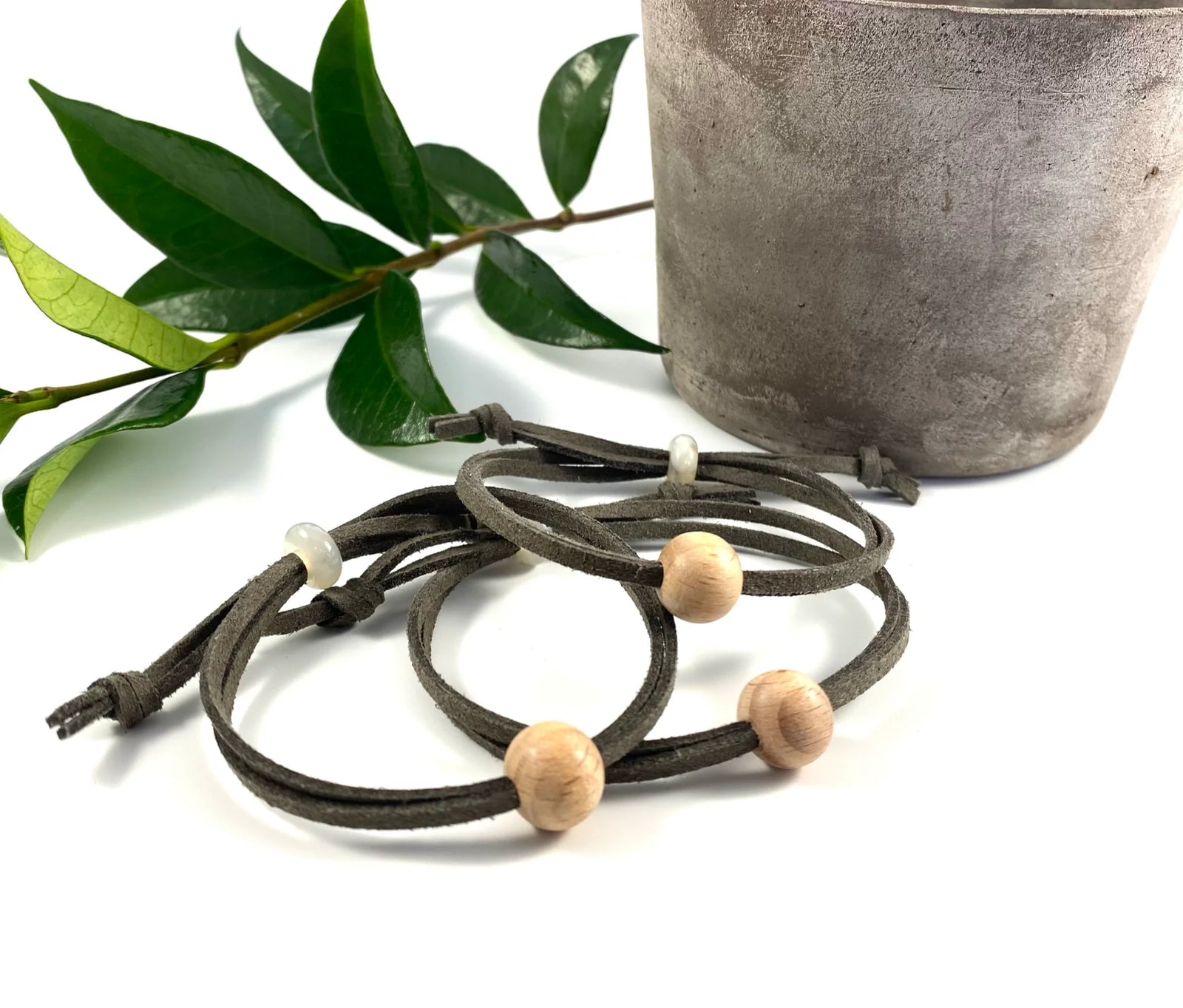 Brown cord anti nausea bracelet with wooden beads and a topaz stone, displayed in front of its branded packaging card on a white surface with a woven basket and green leaves in the background.